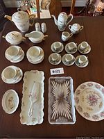 Photo of the full tea set showing teapots, cups, saucers, serving trays, and salt and pepper shakers with floral and gold detailing.