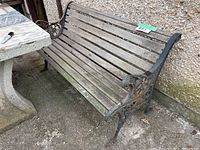 Side angle showing wooden slats and ornate cast iron armrest and leg with signs of rust and wear.