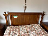 Front view of the solid wood headboard attached to the bed frame with floral patterned mattress, showing the dark wood finish and rounded finials on top of the posts.