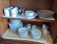 Wide view showing complete set of cups, plates, saucers, serving dish, and goblets arranged on shelves inside cabinet.