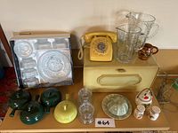 Overview of all items on a table, showing the vintage phone, metal bread box, various glassware items, ceramic teapots, pitchers, and salt and pepper shakers.