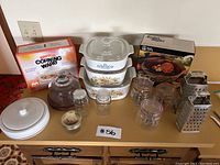 Wide shot showing all items in the lot with Corning Ware dishes stacked in the middle, mason jars, graters, and packaging in background
