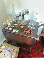 Wide shot showing solid wood drop leaf bar with wheels loaded with various glassware and decanters as well as a decorative item and two small metal bowls with spoons.