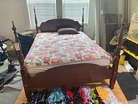 Wooden bed frame with floral bedding, showing full bed with mattress and decorative pillows, surrounded by personal items