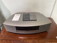 Full view of Bose Wave Music System on wooden surface with two remotes placed on top.