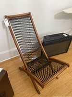 Full view of foldable chair showing wooden frame with multiple horizontal black ropes on seat and backrest.