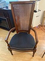 Front view of wooden chair showing cane back and upholstered seat with white piping detail.