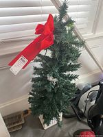 Artificial green Christmas tree approx 40 inches tall with integrated lights, set in plaster pot with damage. Large red bow tied near top.