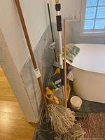 Photo showing the mop bucket, two mops with wooden handles, broom, and hand dustpan next to a bathtub
