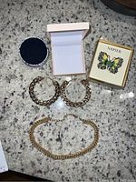 Napier butterfly pin, gold-tone earrings, Sugarfix necklace, and two jewelry boxes on granite surface.