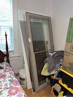 Two metal and glass outer doors leaning against a wall near a window with visible screens (one torn) and loose glass.
