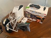 Photo showing Arlo base station, two black Arlo cameras with cables, and Cynoculars VR headset box with remote.