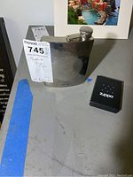 Photo of stainless steel hip flask with screw cap and original markings next to boxed Zippo lighter with logo
