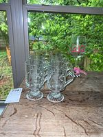 Set of 8 clear glass footed glasses with etched leaf design on table in front of window showing outside greenery.
