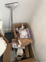 Two filled cardboard boxes with assorted home repair items including wall plates and fire alarm on top