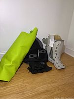 Green yoga mat, Corflex black back brace, black ankle weights, and grey medical boot on floor against wall.