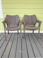 Two brown plastic wicker pattern patio chairs placed on wooden porch floor against yellow wall.