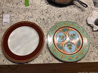 Two Versace by Rosenthal decorative plates on granite countertop, one with turquoise and oriental designs, the other brown with gold trim.