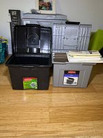 Front view of two Rubbermaid portable file boxes on floor; black box open and gray box with hanging folders on top with paper and envelopes