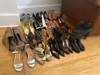 Overall view of 20 pairs of women's shoes including heels, sandals, and two pairs of boots, arranged on a hardwood floor.