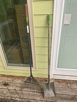 Photo showing the full long-handled rake and blue hawk shovel side by side outside against a green wall and door.