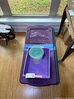 Photo of two stacked Rubbermaid under bed storage bins, one with two wheels, the other with three wheels, plus a small purple tote and a round plastic container on top.