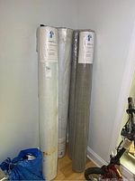 Four rolls of waterproof membrane fabric standing upright against a wall; visible label on white rolls indicates Rainskin LLC waterproof membrane fabrics, styles 10275A and 10175.