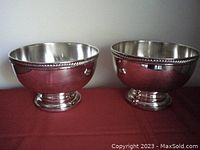 Photo showing two footed silver plated serving bowls side by side on a red surface against a light background.