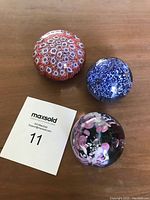 Three paperweights together on wooden surface with lot number card