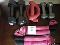 Photo showing all three sets of hand weights and the pink wrist/ankle weights arranged on a wooden surface.