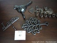 All four decorative wrought iron pieces displayed on a dark wood surface: bird wall hook, cat wall hook, 'Laugh' hook, and vintage trivet.