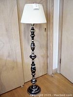 Full view of the floor lamp showing its height, black and brass patterned column and white pleated shade.
