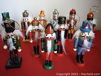Front view of 11 wooden nutcracker Christmas tree ornaments arranged on red surface showing various colors and designs.