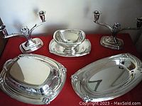 Photo showing the full set with two three-arm candelabra, a covered double vegetable bowl in the center, an oval serving tray on the right, and an oval gravy bowl in front left on red cloth background.