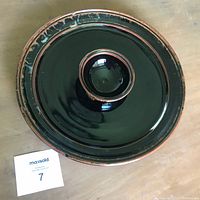 Top view of a round glazed ceramic serving platter with a raised central bowl, black glossy finish with brown edge detail.