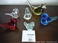 Five glass bird paperweights arranged on a surface showing different colors and styles