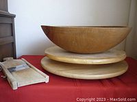 Photo shows large round wooden mixing bowl, two wooden lazy susans stacked beneath it, and vintage wooden Rostfrei mandolin slicer laying nearby on red cloth surface.
