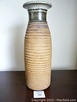 Full front view of the tall studio pottery vase, showing the textured ribbed body and glazed upper neck.