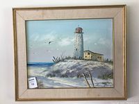 Full view of framed oil painting of lighthouse by the coast with sea birds.