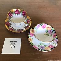 Two Paragon fine bone china tea cup and saucer sets on a wooden surface, showing differing floral patterns and gold trim.