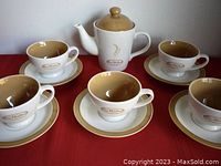 Front view of five Tim Hortons cups on saucers and one teapot placed on red cloth surface.