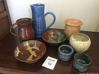 Photo showing all 8 pottery pieces arranged on a table surface with clear view of color and shape variations.