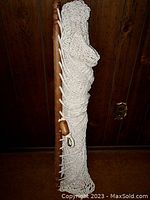 Folded cotton cord hammock showing wooden spreader bar and hook, against wooden paneling.