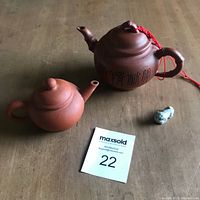 Both Yixing clay teapots displayed on a wooden surface, showing size difference and detail on the calligraphy teapot