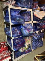 Two white plastic shelving units in a basement filled with blue zipper bags containing assorted items.
