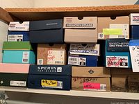 Photo of assorted shoe boxes stacked on shelf, showing various brand labels including Skechers BOBS Memory Foam, Sperry Top-Sider, Cole Haan, and TOMS. Size 8 labels visible on many boxes.