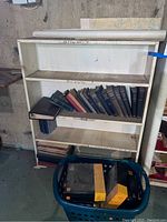 4 shelf white wooden bookcase with books mostly on middle shelves and rolled maps on top.