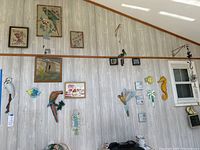 Wide view of the sunporch wall with various framed needlepoint art, metal birds, sea life decorations, and two wind chimes visible.