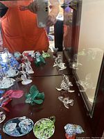 View of mirrored cabinet surface with assorted clear and colored crystal figurines including fish and birds