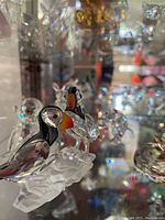 Two tufted puffin crystal figurines side by side on glass shelf